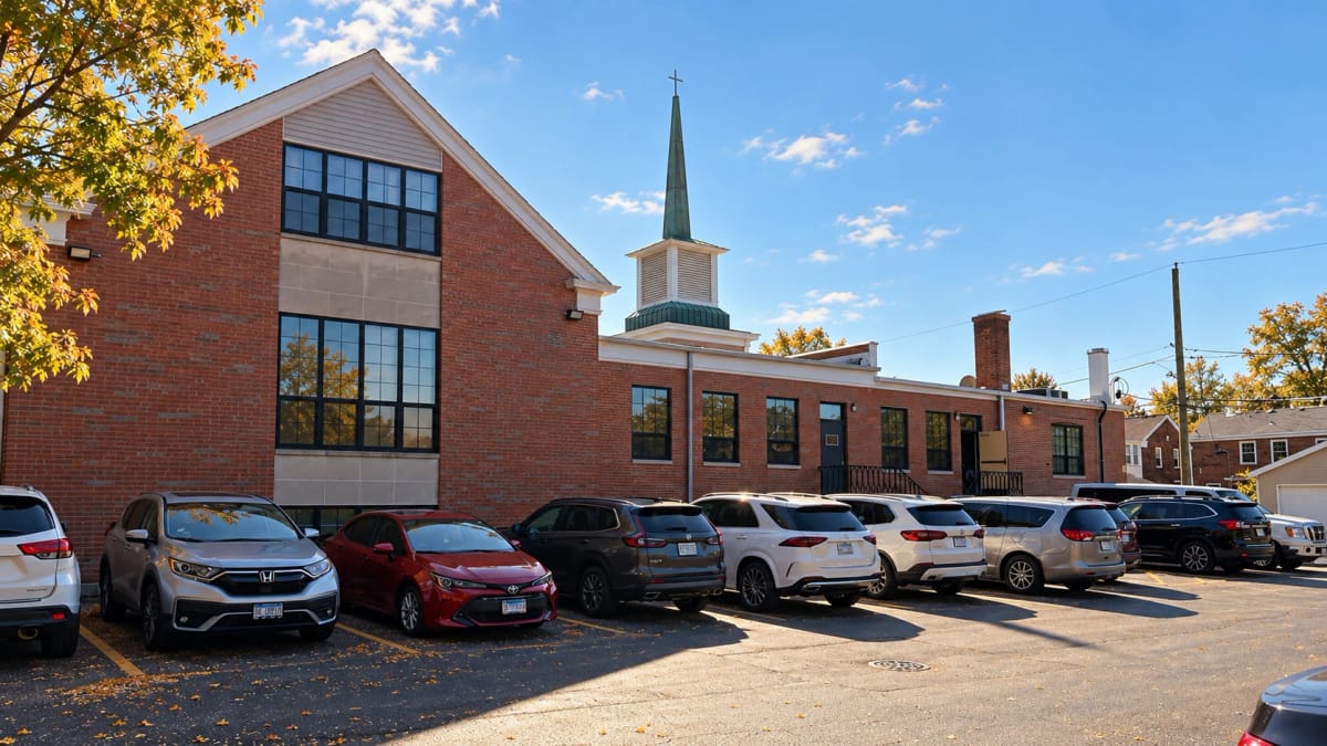 The church’s red brick exterior with a green steeple and the parking lot, in autumn