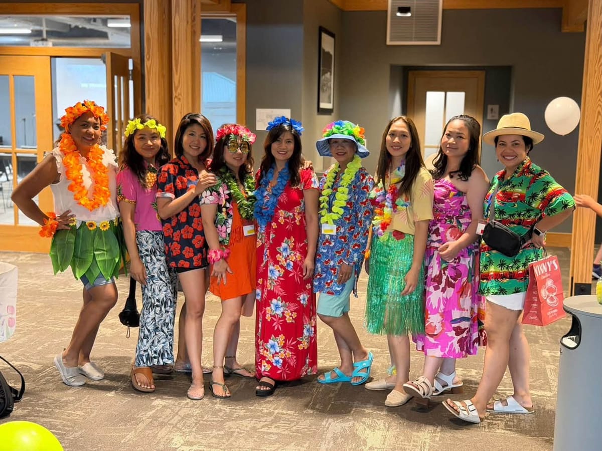 Nine women in flower leis and bright floral outfits posing together at a church event