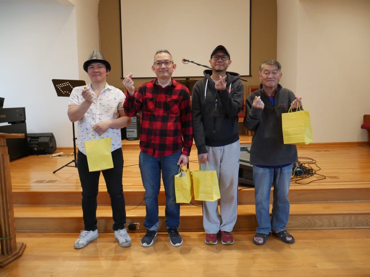 Four men on the sanctuary steps holding yellow gift bags and making finger-heart signs