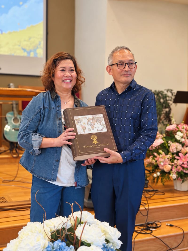 Pastors Malay and David Nattawuttisit standing on the church stage, holding a large book together