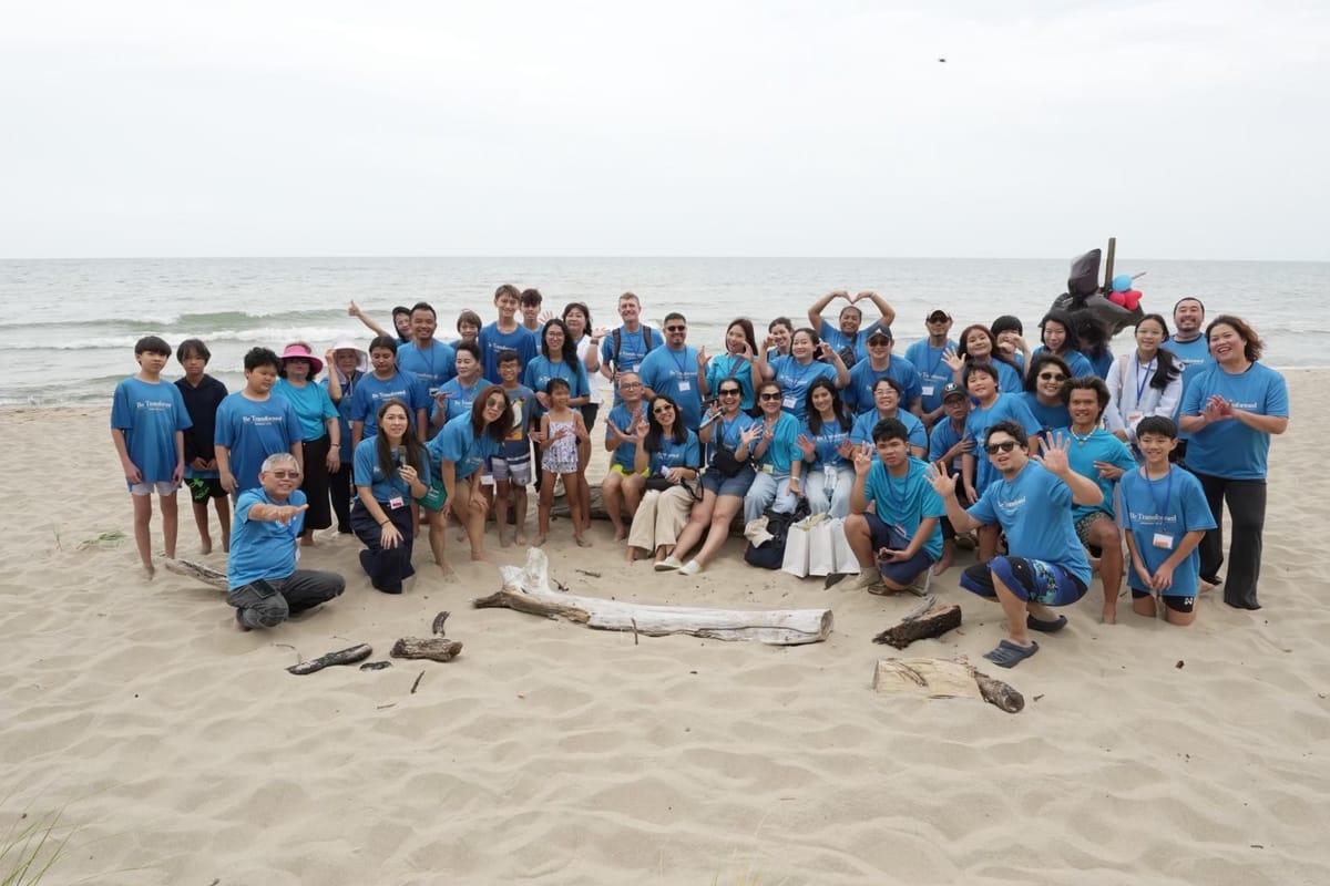 The church family in matching blue Be Transformed shirts, waving and posing on a sandy lakeshore beach